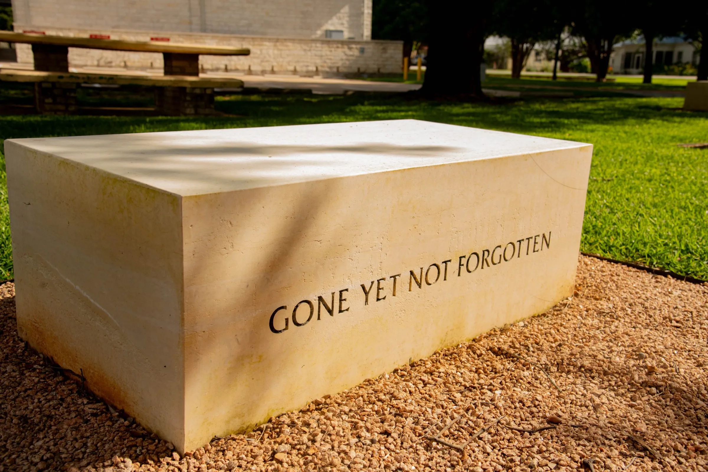 A limestone bench at the memorial engraved “Gone yet not forgotten”