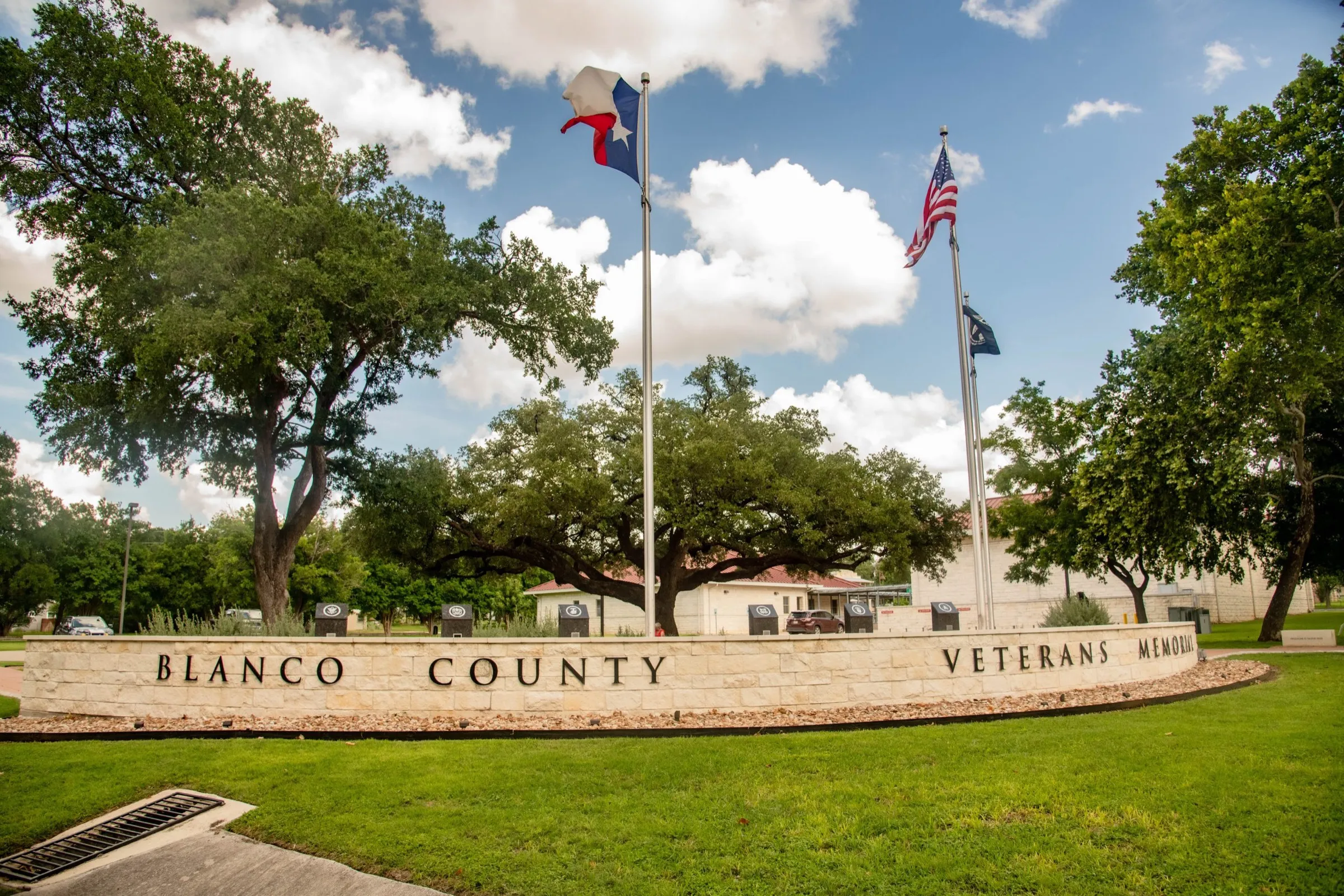 The curved Blanco County Veterans Memorial wall with flags flying under a blue sky